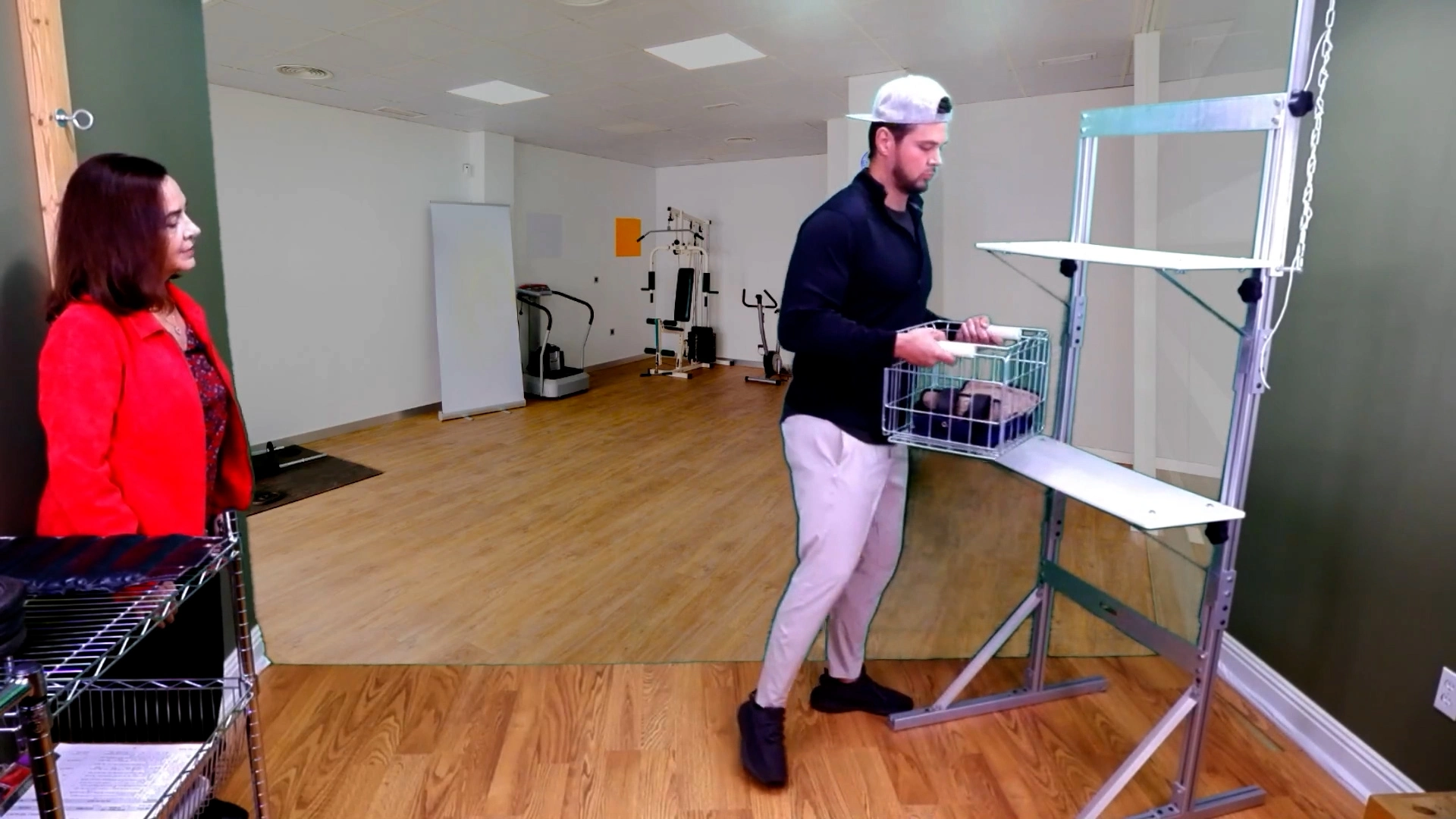 A man is carrying a crate that is weighted for a Job Function Test. He is lifting the crate to a shelf in front of a physical therapist.