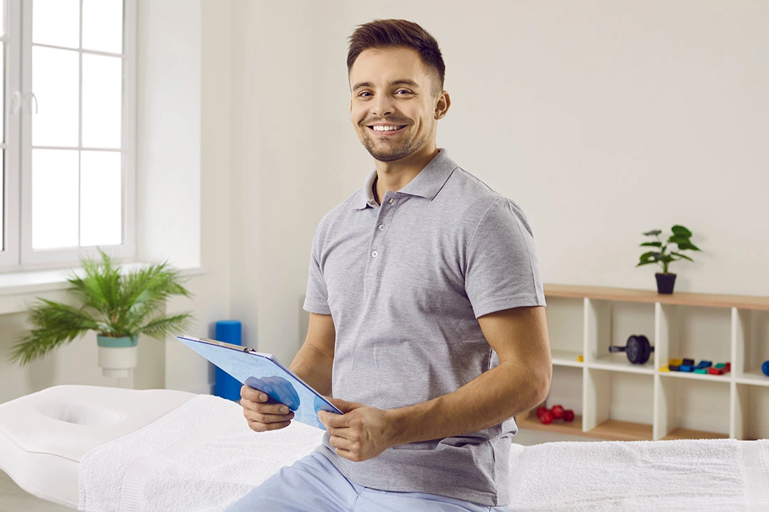 Smiling healthcare professional holding a clipboard in a clean, organized therapy room.