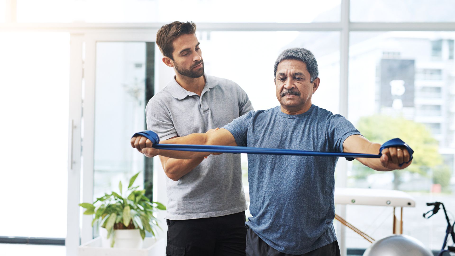 Physical therapist assisting a patient with a resistance band exercise in a rehabilitation setting.