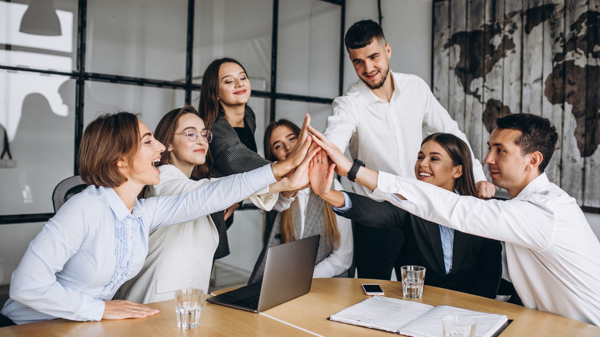 Group of professionals in a meeting giving each other high-fives in celebration.