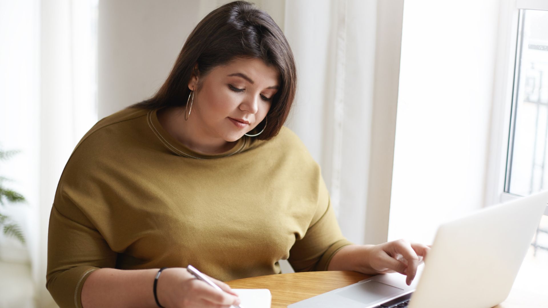 Woman working on a laptop while sitting at a desk in a home office.